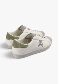 Zapatillas de cuero blancas con acentos de gamuza gris en la punta y el talón. Presentan una calavera y huesos cruzados impresos en el costado, cordones planos y suela texturizada.