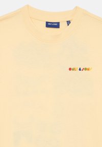 Żółta bawełniana koszulka z okrągłym dekoltem i wielokolorowym logo "ONLY & SONS" na lewej piersi. Miękka faktura.