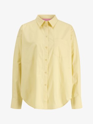 Jasnożółta koszula na długi rękaw z zapięciem na guziki, pojedynczą kieszenią na piersi, klasycznym kołnierzykiem i zaokrąglonym dołem, prezentowana na białym tle.