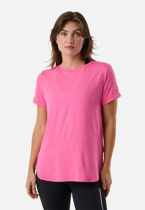 Frau trägt ein leuchtend pinkes T-Shirt mit kurzen Ärmeln und schwarze Leggings, steht vor einem einfarbigen weißen Hintergrund.