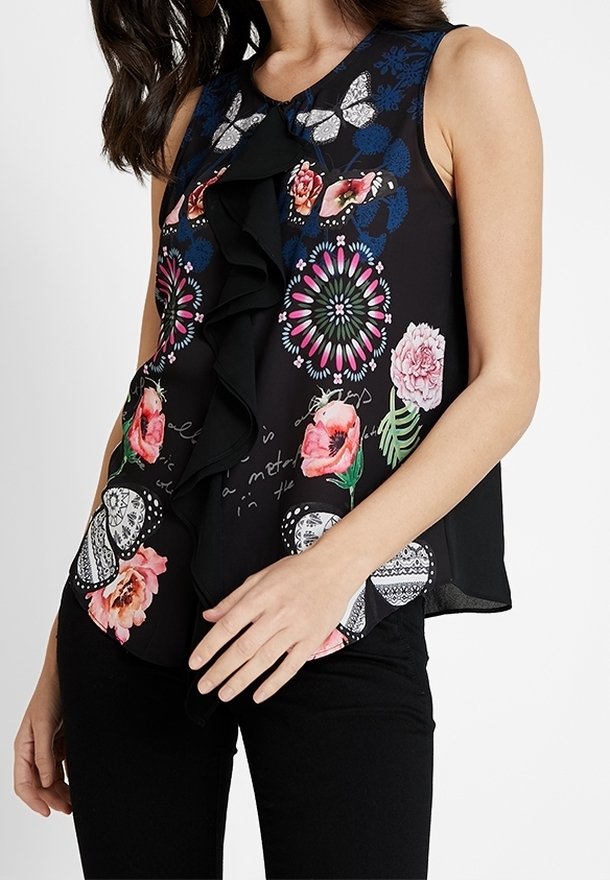 Haut noir sans manches avec motifs floraux et papillons colorés ainsi qu'un détail volanté sur le devant, porté avec un pantalon noir.