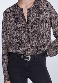 Langärmelige, knöpfbare Bluse im beige und schwarzen Leopardenmuster, mit rundem Ausschnitt und lässiger Passform, kombiniert mit schwarzen Jeans und einem Gürtel.