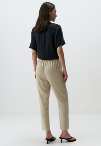 Top nero a maniche corte con vestibilità rilassata, abbinato a pantaloni beigi elasticizzati in vita. Il modello indossa sandali neri con tacco e cinghie.