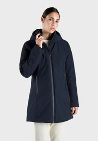 Navyblauwe waterdichte jas met een capuchon, voorzien van een ritssluiting aan de voorkant, twee zijzakken en een gladde textuur. Ontwerp met een lengte tot halverwege de dijen.