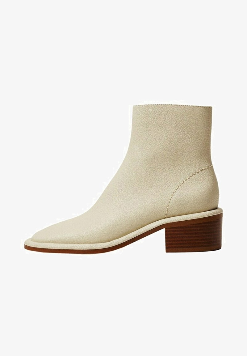 Bottine en cuir beige avec un bout pointu, une surface texturée et un talon carré en bois. Détails de couture simples le long des bords.