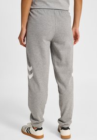 Grå sweatpants med elastisk midja, med vita chevrondetaljer på sidorna och nedhasade benslut. Bärs med vita sneakers.