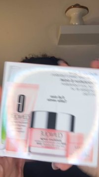 Emballage til hudplejeprodukt med en lyserød krukke med sølvlåg, et hvidt rør og en farverig holografisk detalje. Mærkater er synlige.