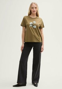 T-shirt en coton vert olive à manches courtes avec un imprimé floral. Assorti à un jean noir à pattes d'éléphant et des chaussures noires à enfiler.