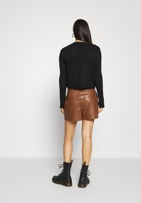 Suéter negro de canalé, pantalones cortos de cuero marrón y botas negras de cordones con acentos amarillos. Textura suave y diseño ajustado.