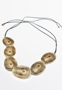 Collana color bronzo con sei pendenti ovali su cordino nero. Superficie testurizzata con indentazioni centrali. Chiusura regolabile alle estremità.