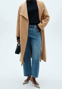 Velbloudí kabát se širokým límcem, černý rolák, světlé modré džíny s vysokým pasem a béžové lodičky s špičatou špičkou. Jako doplněk černá kabelka.