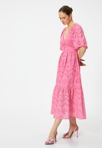 Roze midi-jurk met puffmouwen, oogjespatroon, gelaagde zoom en aansluitend lijfje. Gemaakt met lichtroze sandalen met hakken met bloemenaccenten.