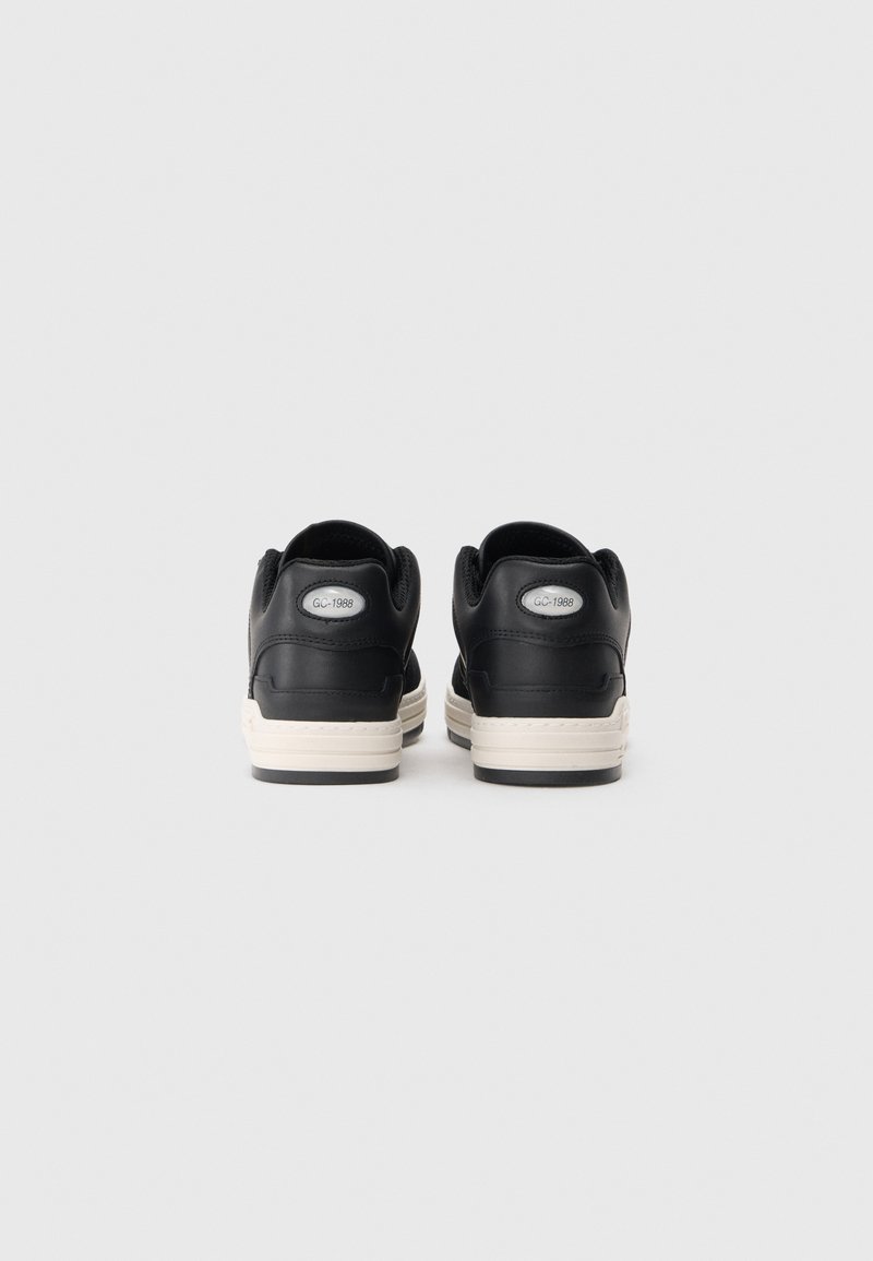 Black leather sneakers with a smooth finish, white rubber soles, and a logo detail on the heel. Low-top design with rounded edges.