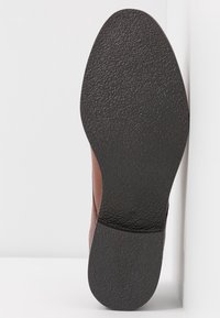 Chaussure en cuir marron avec une semelle en caoutchouc noir texturé ; présente une surface lisse et une étiquette de taille discrète sur le côté.