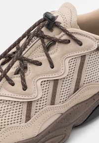 Beige sneakers med en kombination av mocka och mesh-material, med bruna accenter, texturerade overlay och en dämpad sula.