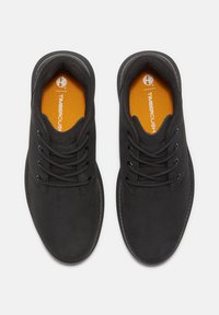 Zapatos de cuero negro con textura suave y punta redonda. Presentan cordones, un cuello acolchado y una plantilla naranja con marca.