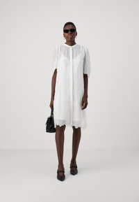 Rochie albă scurtă cu mâneci pufoase transparente, material texturat, margine ondulată, asortată cu o geantă neagră și pantofi cu vârf ascuțit. Ochelari de soare purtați.