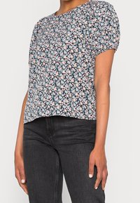 Top floreale a maniche corte in blu navy, con un denso motivo di fiori rosa e blu su uno sfondo scuro. Tessuto morbido, scollatura rotonda.