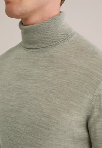 Svetlozeleni pulover s turtleneck iz teksturirane pletenine. Oprijeten ovratnik in gladka površina s subtilnimi variacijami v barvi.