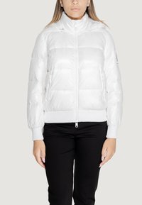 Giacca a vento bianca in stile puffer con cuciture orizzontali, colletto alto, zip frontale e tasche laterali. I polsini e l'orlo a coste completano il design.