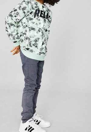 Sweatshirt vert menthe à col rond avec le texte noir "RELAX", associé à un pantalon gris slim-fit et des sneakers blanches avec des accents noirs.