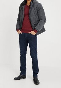 Graue gepolsterte Jacke mit Kapuze, burgunderroter V-Ausschnitt-Pullover, dunkelblaue Jeans und schwarze Ankle Boots. Figurbetontes Design mit Reißverschluss und Taschen.