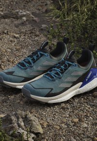 Blue and gray athletic shoes feature a textured mesh upper, contrasting black accents, and blue laces. The sole is white with a rugged tread.