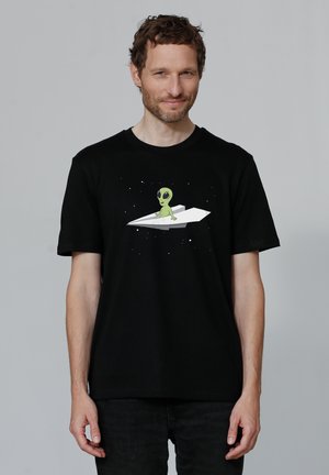 Zwarte katoenen T-shirt met een grafiek van een groene alien op een papieren vliegtuigje tegen een sterrenachtige achtergrond. Korte mouwen, ronde hals.