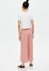 T-shirt blanc court avec ourlet festonné, associé à un pantalon large rose clair. Porté avec des baskets noires ornées d'accents colorés.