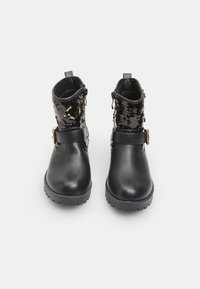 Botas de tobillo de cuero negro con parte superior de lentejuelas negras brillantes y una correa con un hebilla dorada alrededor del tobillo. Suela de goma texturizada.