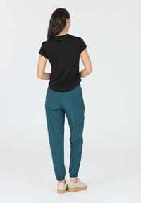 Schwarzes kurzärmeliges Oberteil und türkisfarbene Jogginghose mit elastischen Bündchen. Glatter Stoff, lockere Passform, minimalistische Details. Die Schuhe sind beige mit einer dicken Sohle.