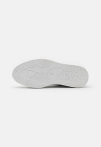 Suela de zapato de goma blanca con patrones texturizados y logotipo "Calvin Klein" troquelado. Presenta estrías para mayor agarre. Acabado suave.