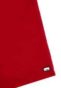 Punaiset sortsit, jotka on valmistettu sileästä kankaasta, jossa on näkyvä ruutukuvio. Alakulmassa on musta etiketti.