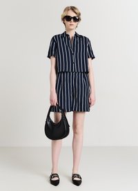 Completo a due pezzi a righe blu navy e bianche con maniche corte e pantaloni shorts, abbinato a una borsa a tracolla nera e a delle scarpe ballerine a punta con dettagli in borchie.