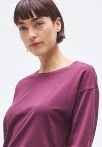 Μωβ πουκάμισο μακριάς μανίκας από απαλό ύφασμα, με στρογγυλή λαιμόκοψη και χαλαρή γραμμή, με ορατές ραφές και απαλή υφή.