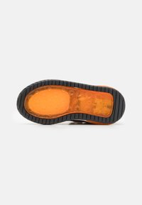 Semelle en caoutchouc noire avec un intermédiaire orange, présentant des textures circulaires et un bord extérieur noir texturé, conçu pour améliorer la traction.