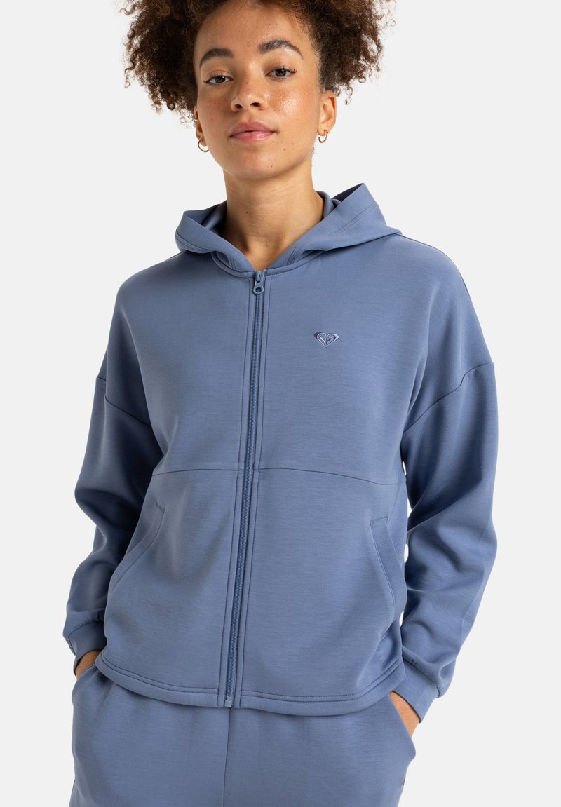 Svetlomodrá mikina na zips vyrobená z textúrovaného materiálu, s predným vreckom, kapucňou a malým logom na hrudi. Uvoľnený strih.