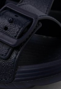 Sandal blu scuro con tomaia sintetica testurizzata, cinturino regolabile con fibbia e suola ammortizzata con un sottile motivo a onde.