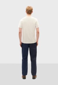 Herren T-Shirt mit kurzen Ärmeln in Creme und marineblauen Hosen, die einen klassischen Schnitt mit geradem Bein, minimalistisches Design und weichen Stoff aufweisen.