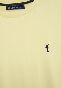 T-shirt à col rond jaune clair avec étiquette noire "POLO CLUB" et petit logo de joueur de polo brodé en noir sur la poitrine.