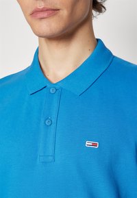 Polo shirt in cotone blu con una finitura testurizzata, dotato di colletto, due bottoni e un piccolo emblema logo tricolore sul petto.