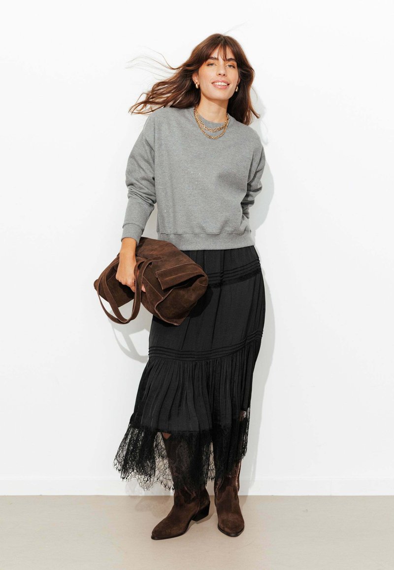 Sweat-shirt gris, jupe noire à étages avec bordure en dentelle, sac en daim marron et bottines en daim assorties. Design simple et tissu texturé.