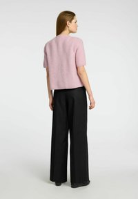 Roze trui met korte mouwen in een losse pasvorm, gemaakt van zacht, pluizig materiaal, gecombineerd met brede zwarte broeken. Eenvoudig, modern ontwerp.
