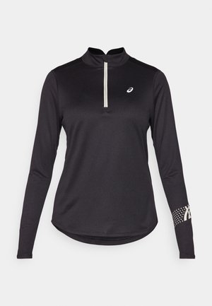 Haut de sport noir à manches longues avec col à demi-zip, tissu texturé et motif à pois sur la manche droite avec des accents de logo.