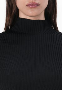 Svart ribbestrikket turtleneck med en tettsittende design og vertikale striper. Stoffet er glatt og elastisk, noe som forbedrer den generelle teksturen.