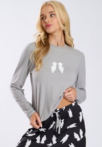 Camisa de manga larga gris con un gráfico de un oso polar juguetón en el pecho, combinada con pantalones cortos negros que presentan un patrón de osos polares blancos.