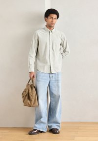 Svetlo zelena srajca z dolgimi rokavi in žepom, v kombinaciji s širokimi modrimi kavbojkami. Rjavi usnjeni čevlji in bež torbica.