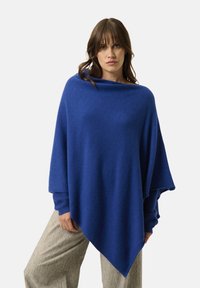 Blå strikket poncho med en afslappet pasform, der har en bred halsudskæring og lange ærmer, lavet af blødt, varmt stof. Glat tekstur.