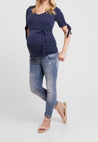 Marinblå v-ringad topp med korta ärmar och knytning vid midjan, tillsammans med ljusblå skinny jeans och beige band sandaler.