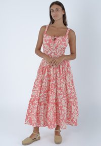 Abito maxi floreale rosa con un corpetto aderente e gonna a strati. Presenta spalline regolabili e un dettaglio con fiocco sul collo.